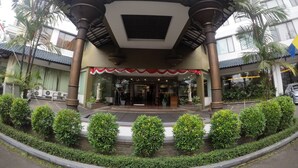 A covered entrance with a tiled roof, a stone base, and a decorative awning. - Kedaton Hotel (Bandung)
