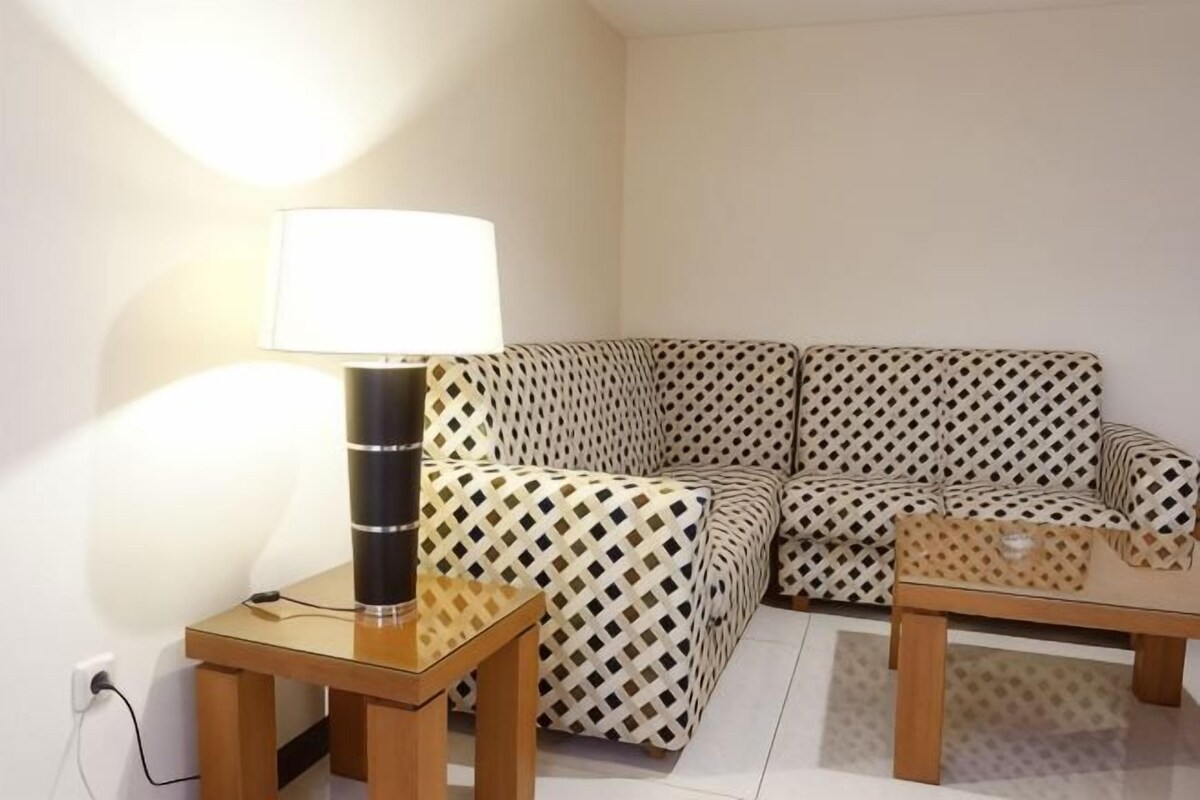 A living room with a patterned sofa, a side table with a lamp, and a small wooden table.