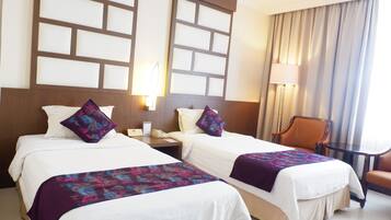 Ein Hotelzimmer mit zwei Betten, einem Schreibtisch, einem Stuhl und einem großen Fenster mit Vorhängen.