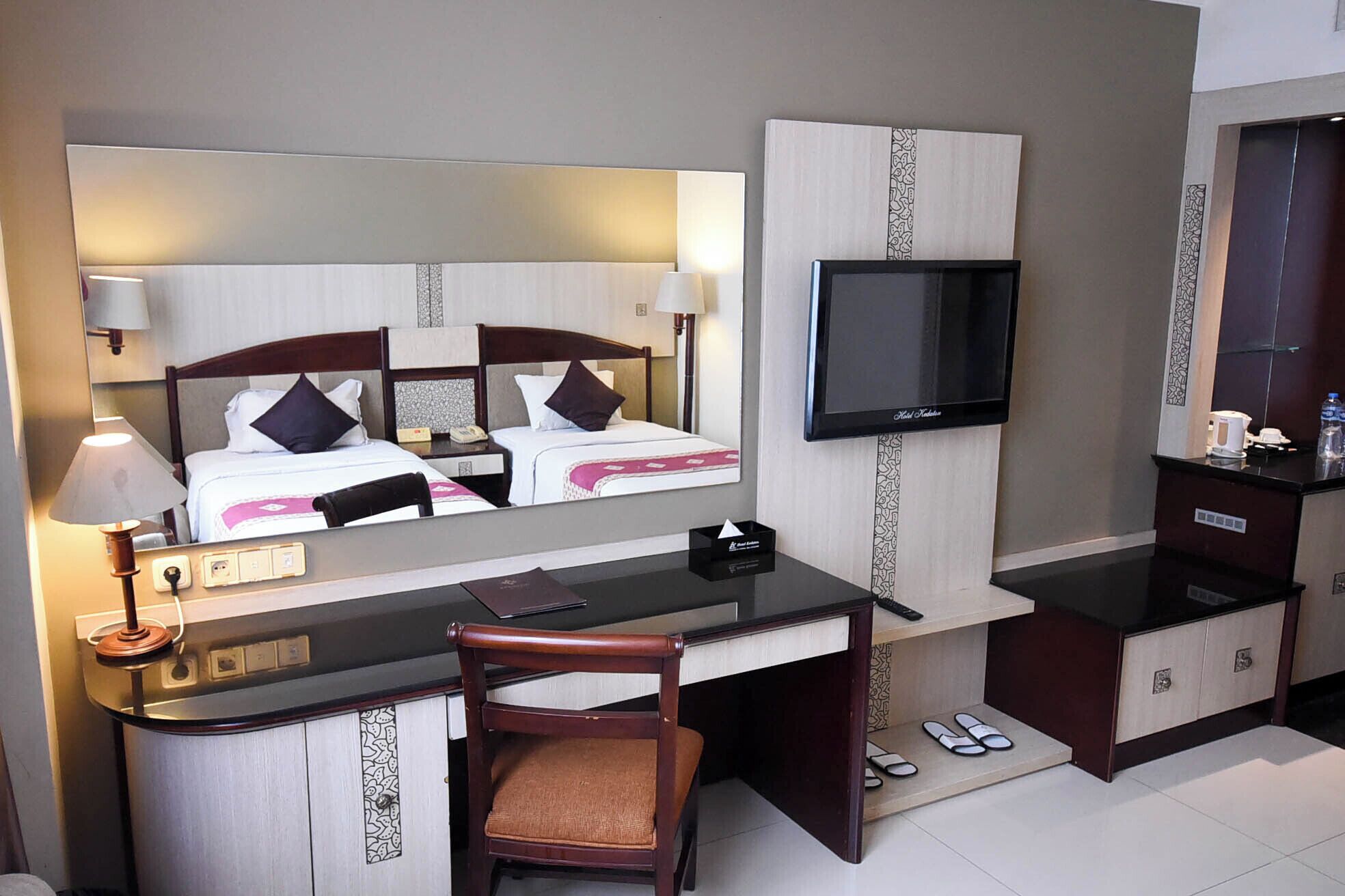 A hotel room with a bed, a desk, a chair, a TV, and a minibar.
