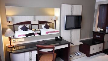 A hotel room with a bed, a desk, a chair, a TV, and a minibar.