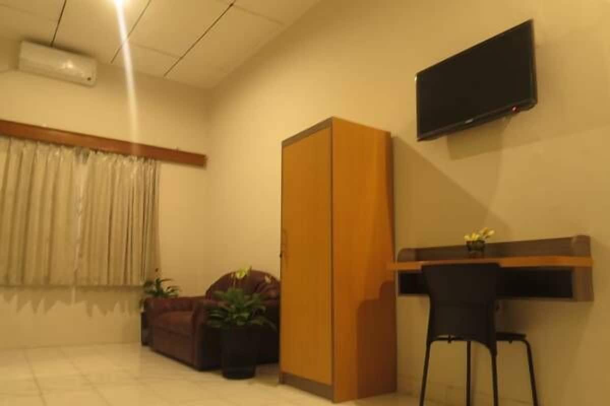 A room with a desk, chair, wardrobe, and a flat-screen TV mounted on the wall.