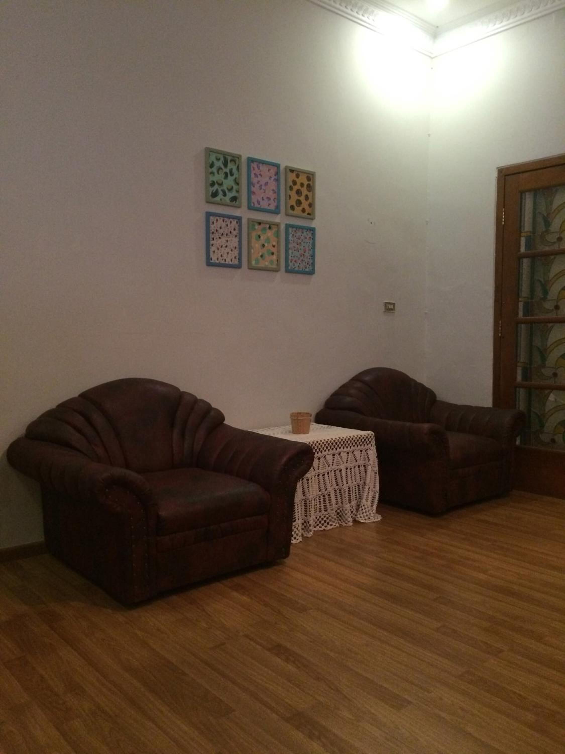 A living room with two brown leather sofas, a small white table with a basket, and a wall with six framed artworks.