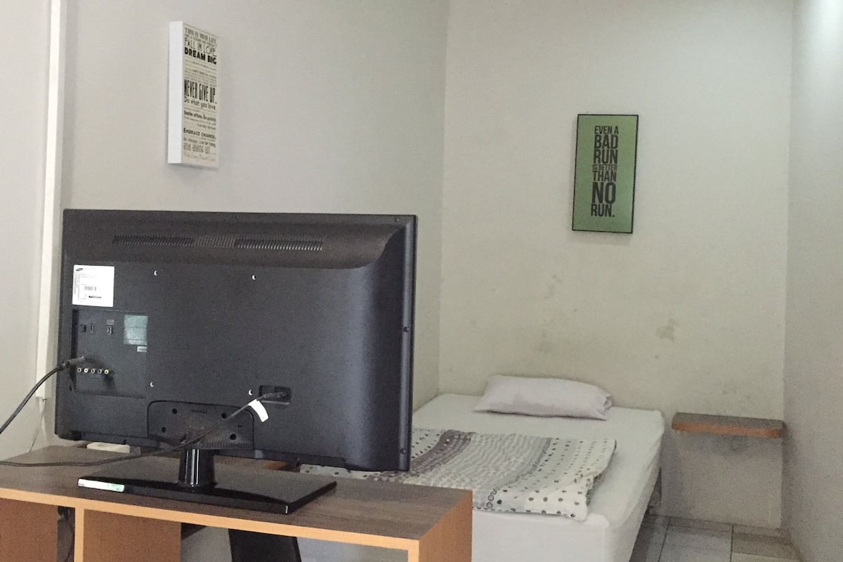 A small, simple room with a bed, a television on a wooden stand, and a small table.