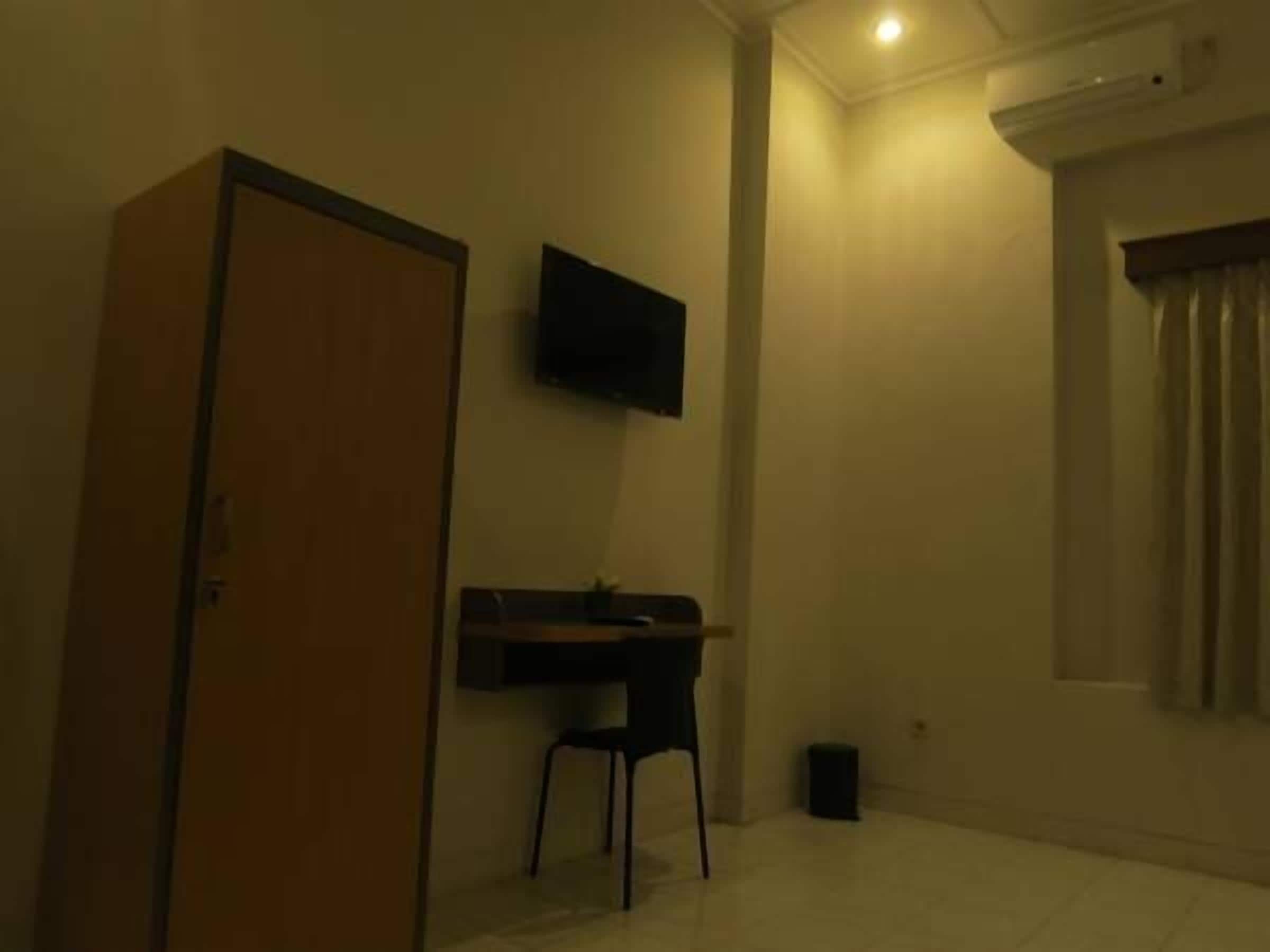 A room with a wooden door, a desk with a chair, a mounted TV, and a window with curtains.