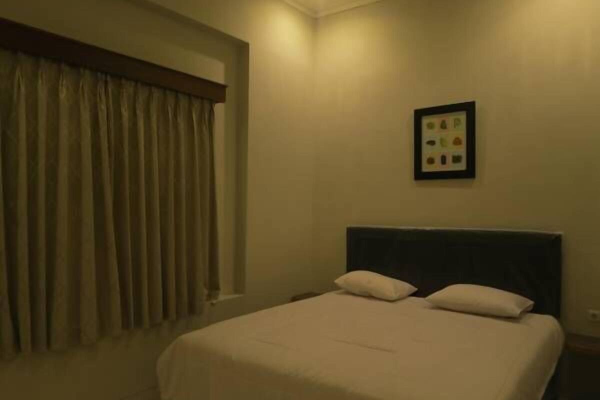 A bedroom with a bed, a window with curtains, and a framed picture on the wall.