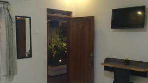 Un dormitorio con cama, escritorio, silla, televisión y puerta que da a un balcón.