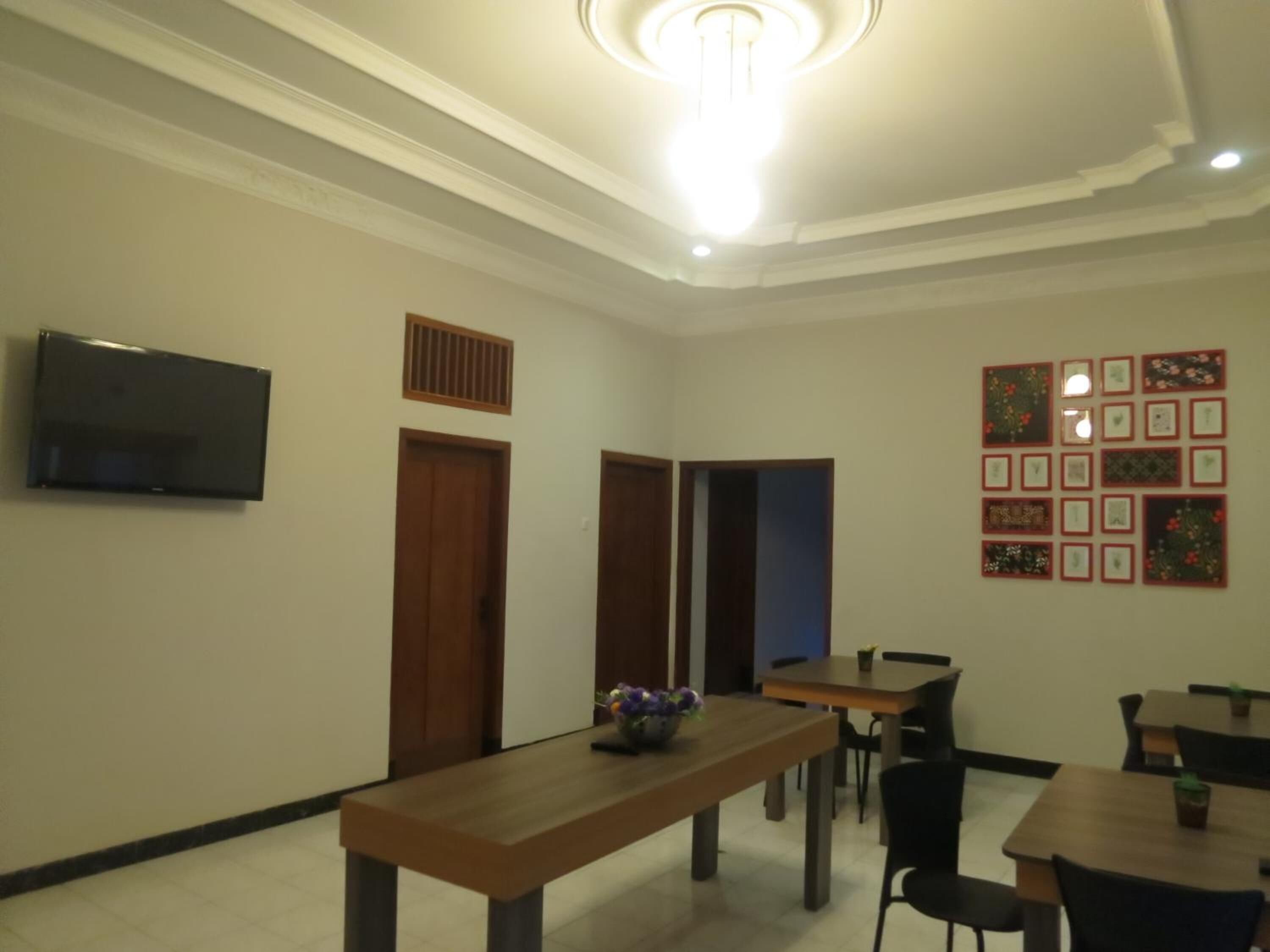 A dining area with a long wooden table, several chairs, a television mounted on the wall, and framed pictures on the wall.