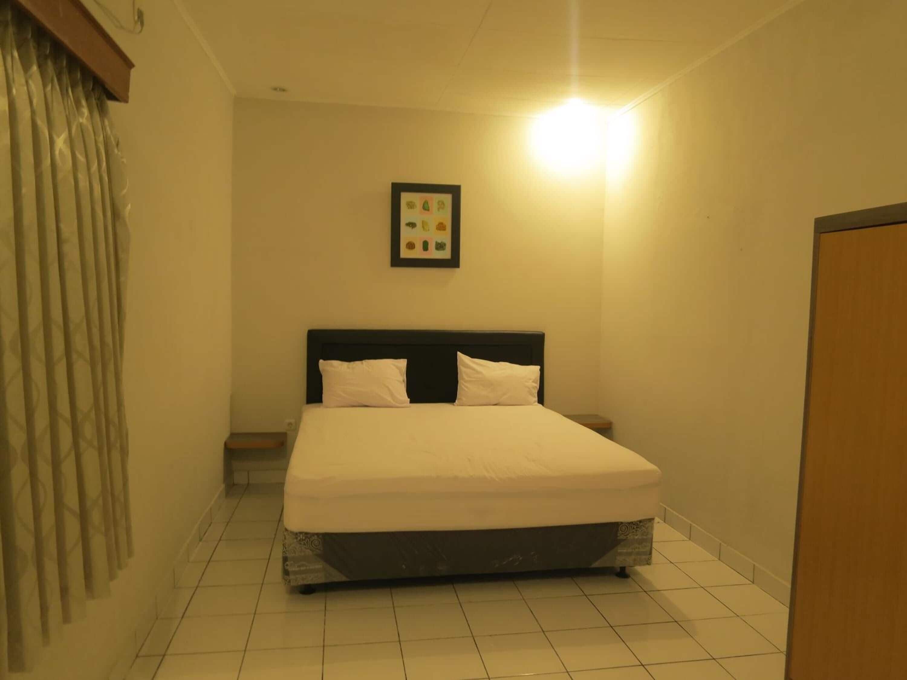 Une chambre à coucher avec un lit, une table de chevet, un tableau encadré au mur et une porte.