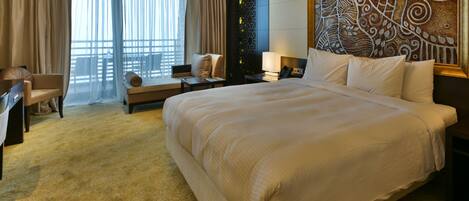 A large bed with a headboard, a desk, a chair, and a window with curtains.