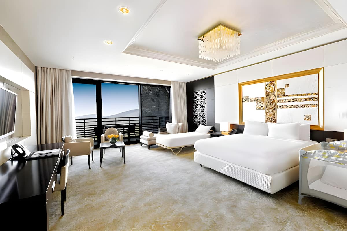 A modern hotel room with a large bed, a desk, a chair, and a view of the outdoors.