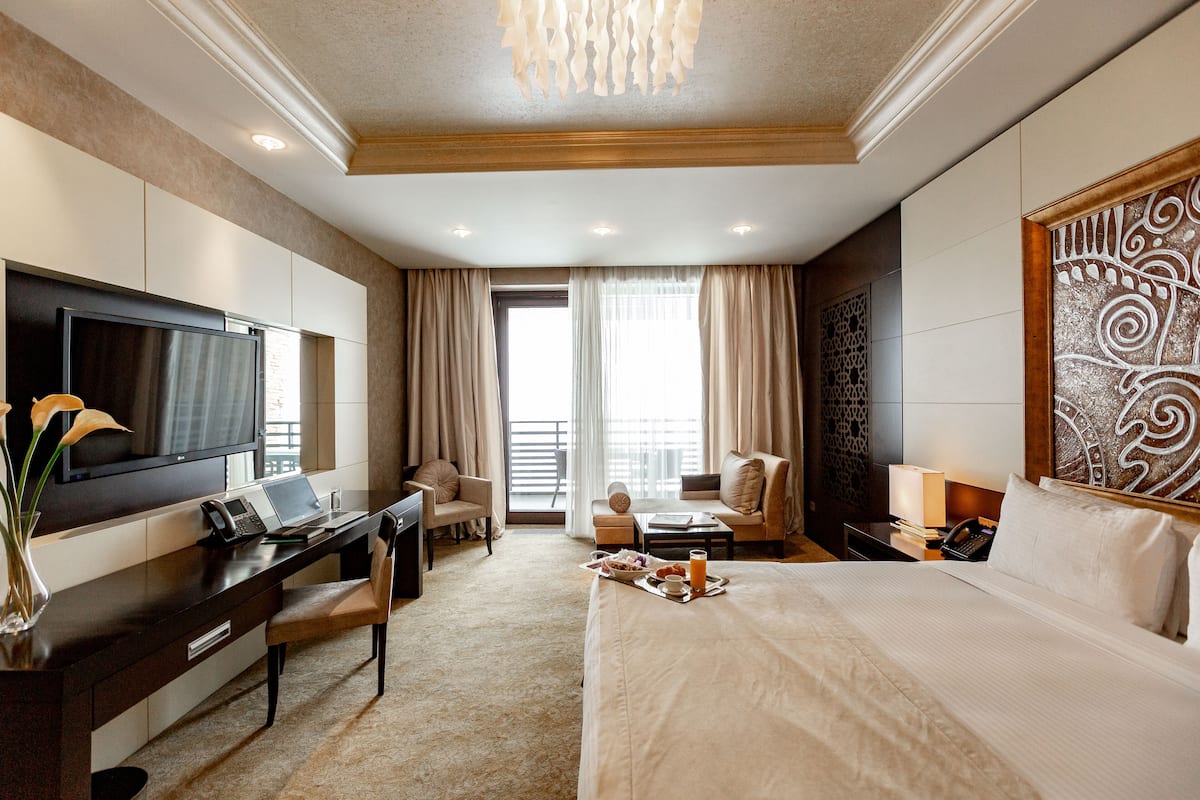 A hotel room with a bed, desk, TV, and a view of the outdoors.