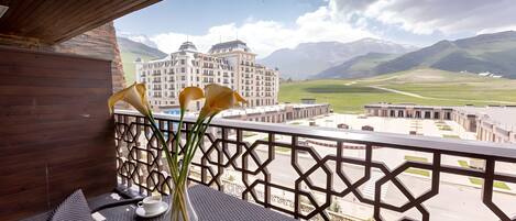 A balcony with a table, a vase with flowers, and a view of a hotel and mountains.