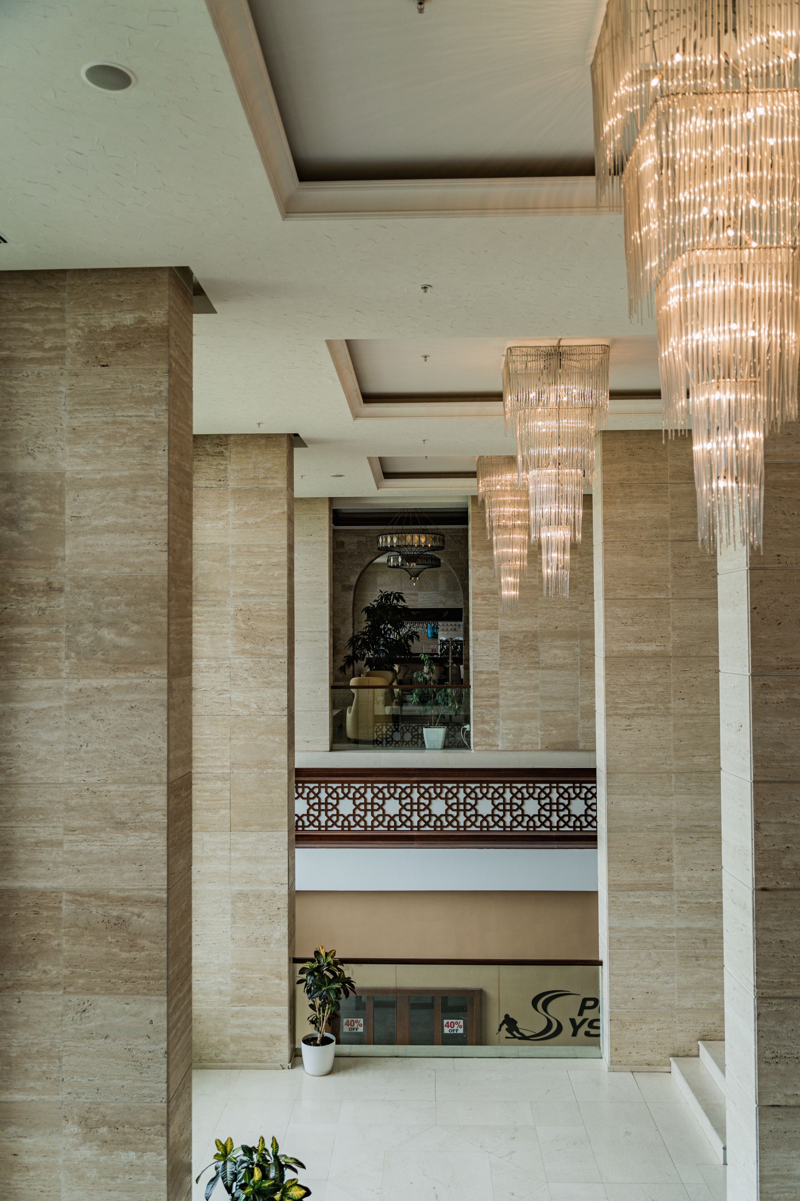 A spacious lobby with a high ceiling, a large chandelier, and a view of a second-floor balcony with a railing.