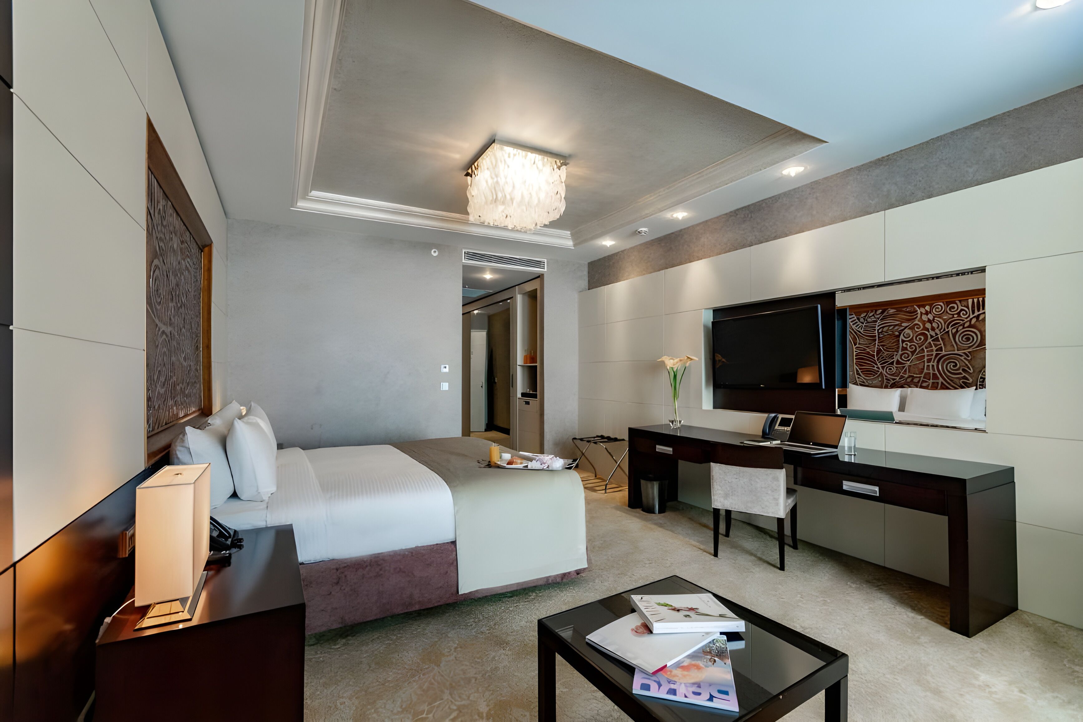 A hotel room with a bed, desk, TV, and a chandelier.