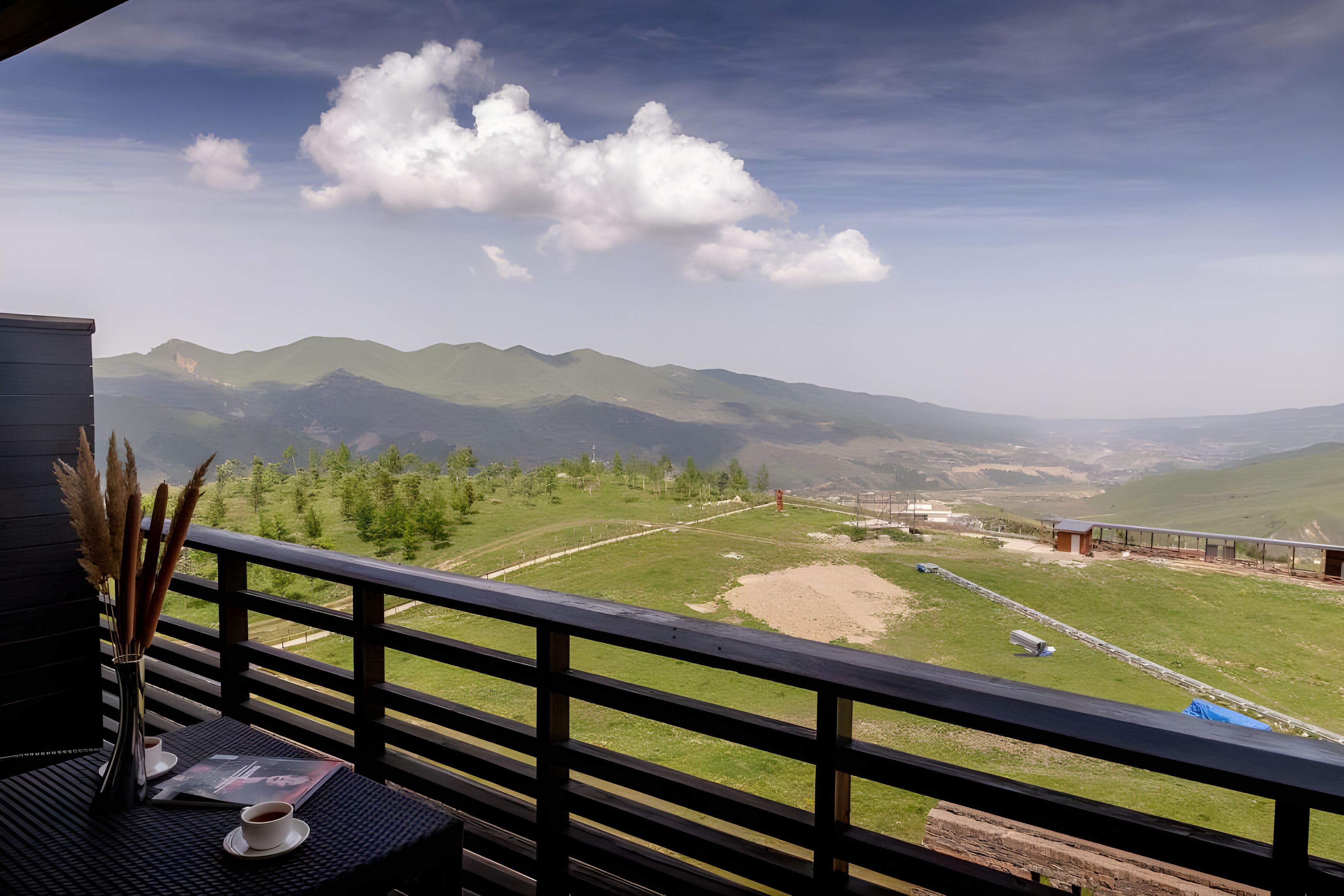 Ein Balkon mit Blick auf Berge, ein Tisch mit einer Vase und einer Tasse, sowie ein Buch.