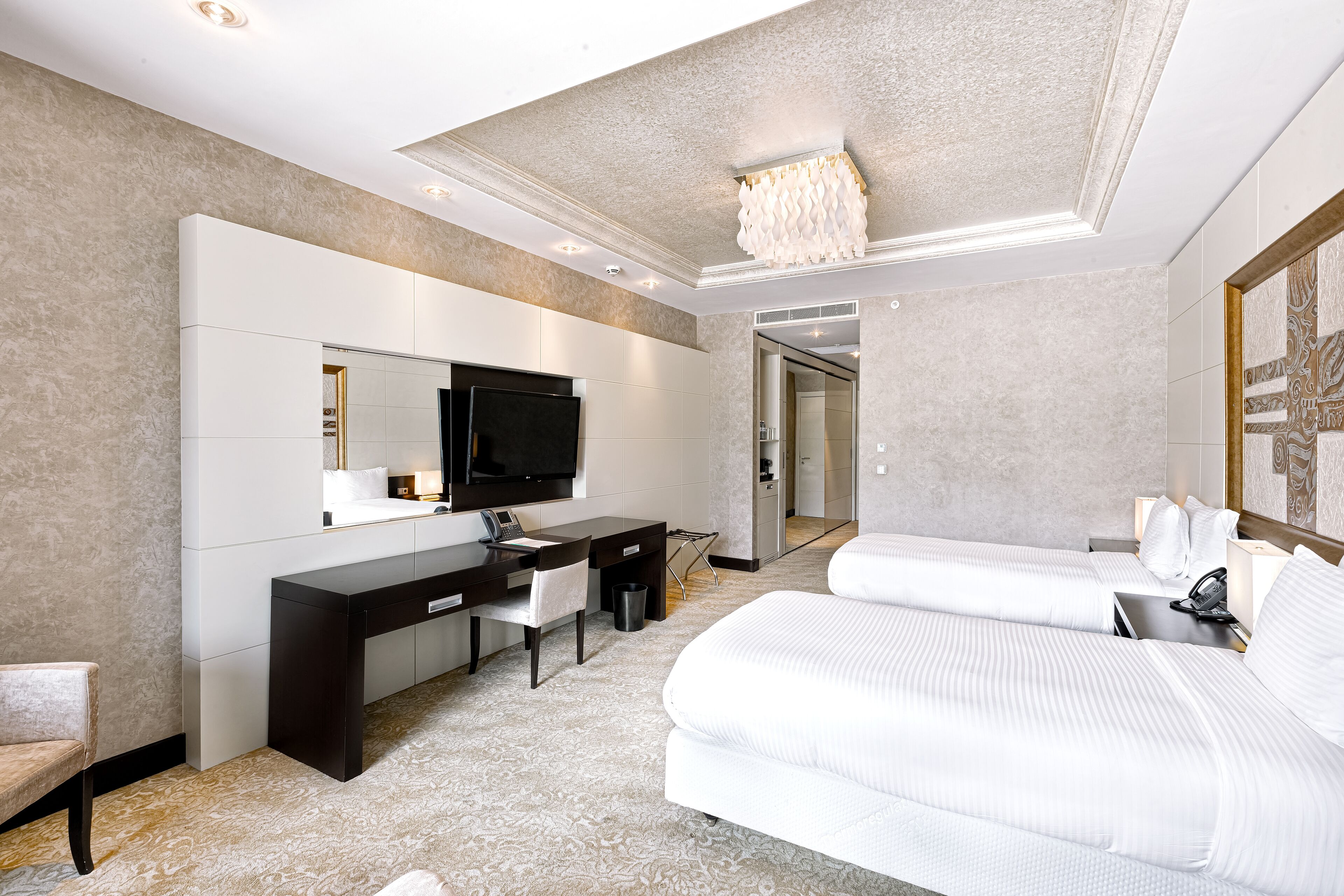 A modern hotel room with a large bed, a desk with a chair, a television, and a bathroom visible through an open door.