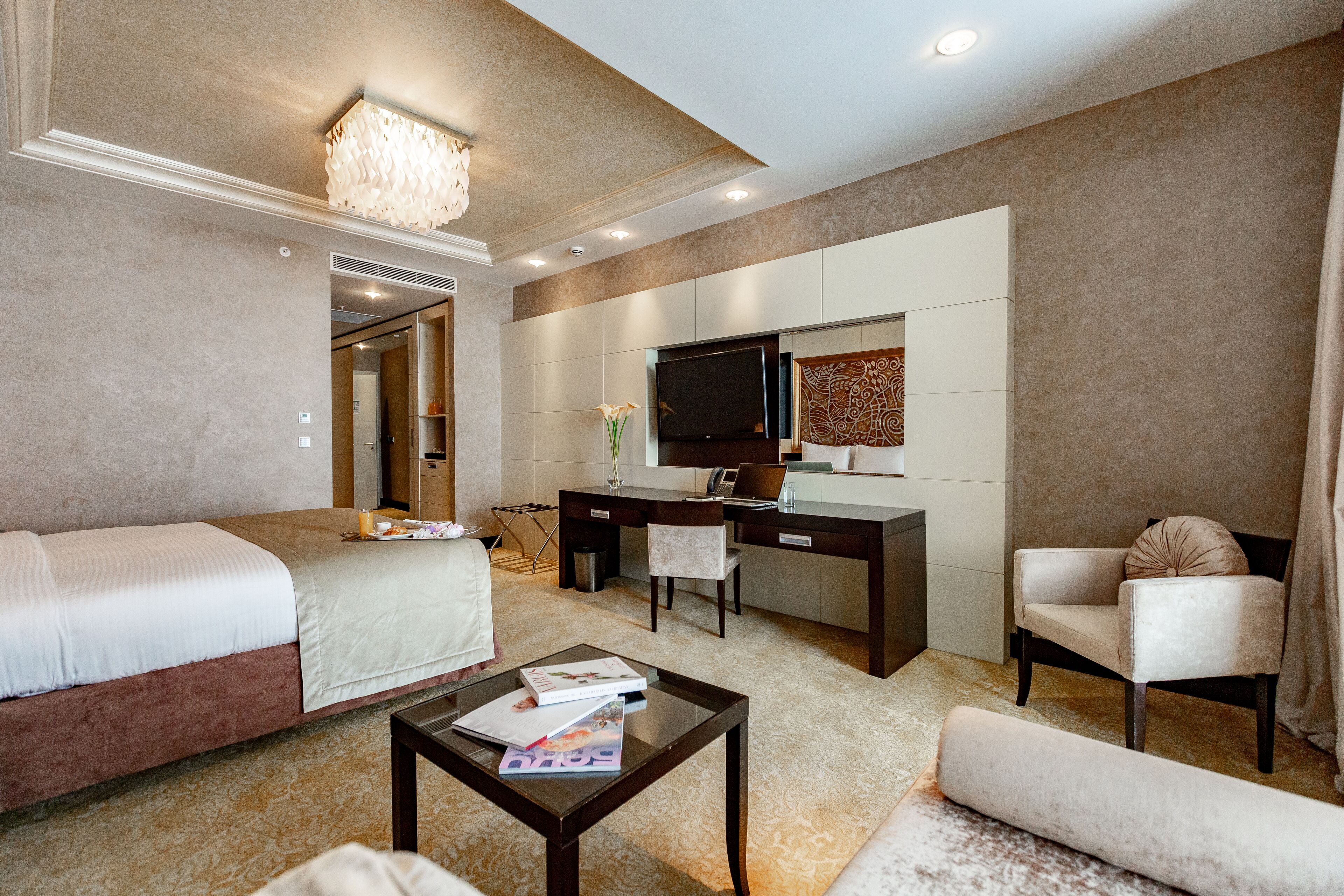 A hotel room with two beds, a desk, a chair, a coffee table, and a TV.