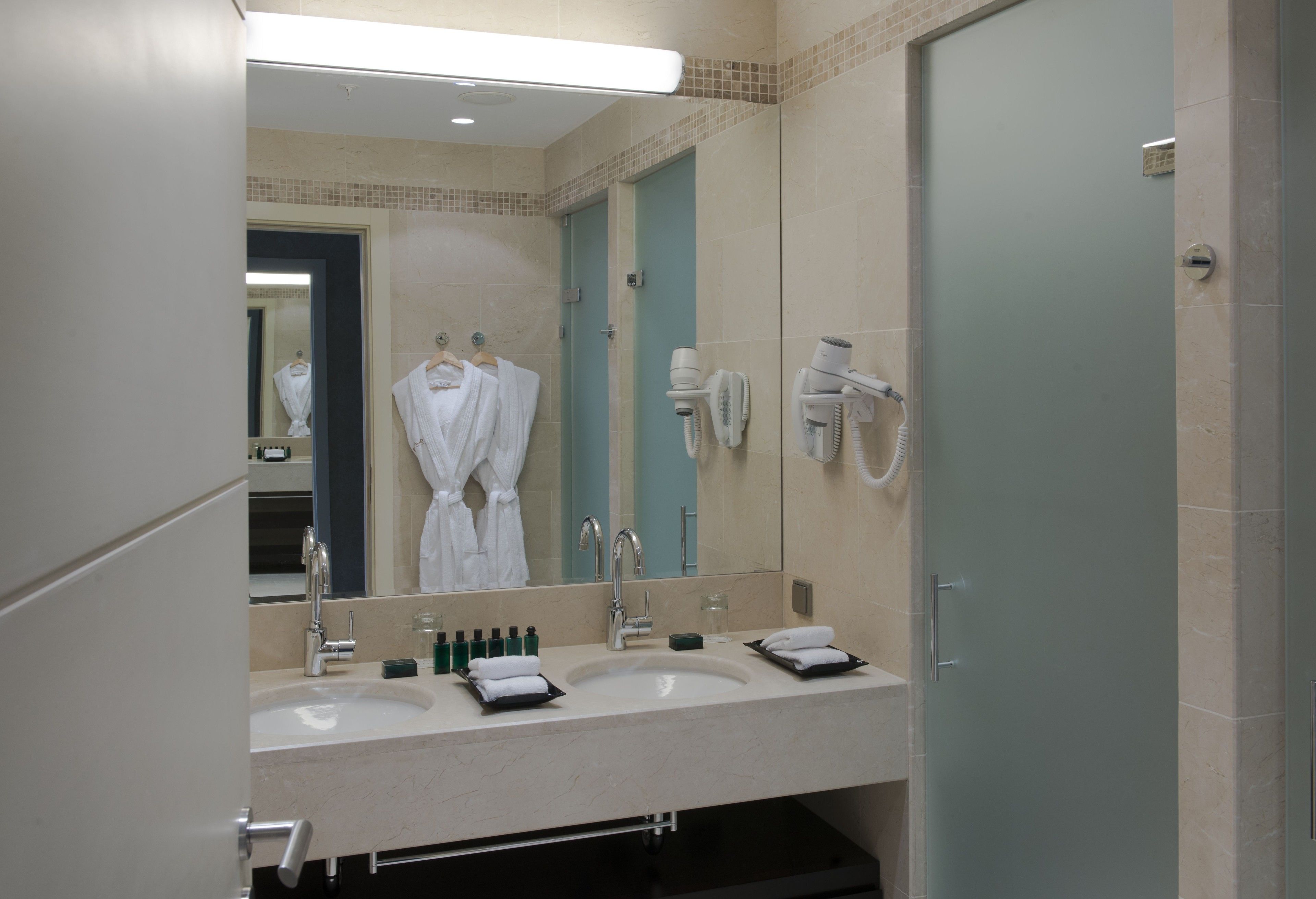 Een hotelbadkamer met twee wasbakken, een spiegel, een haardroger en een handdoekrek.