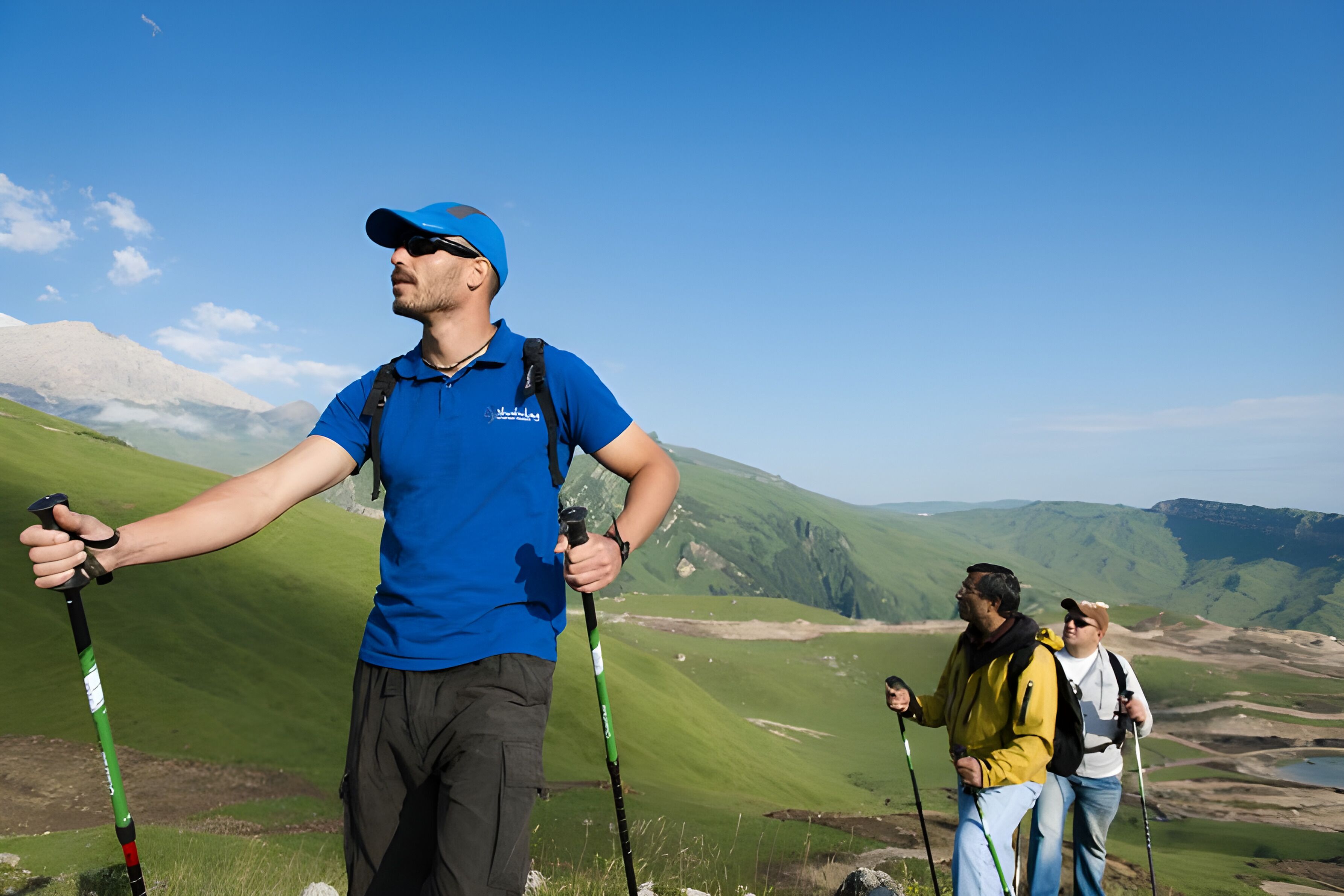 A hiker with a backpack and trekking poles on a grassy hill with a clear sky.