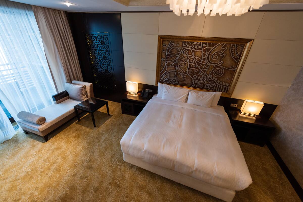 A hotel room with a large bed, a sofa, a desk, and a decorative headboard.