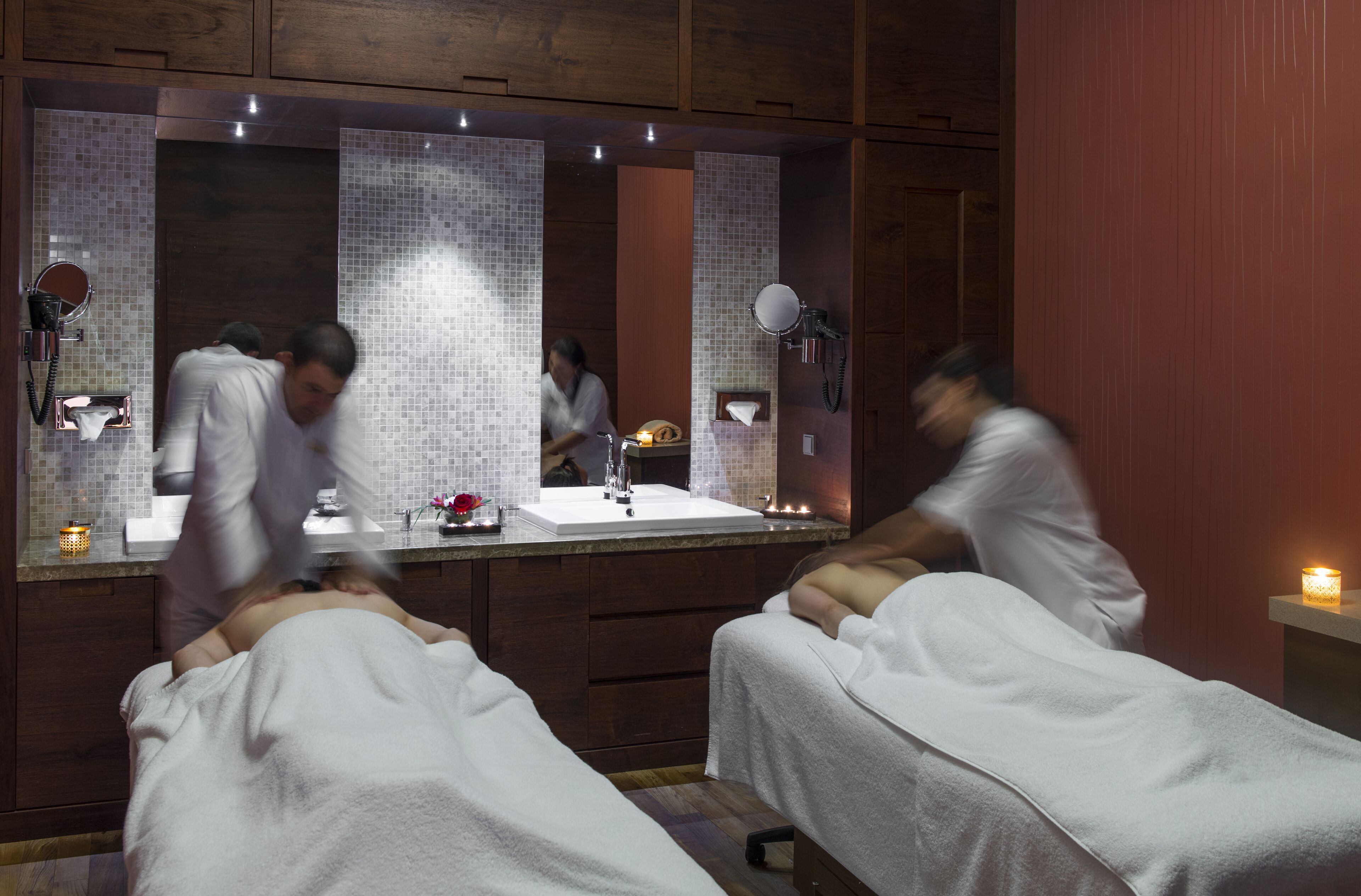 A spa room with two massage tables, a large mirror, and a sink.