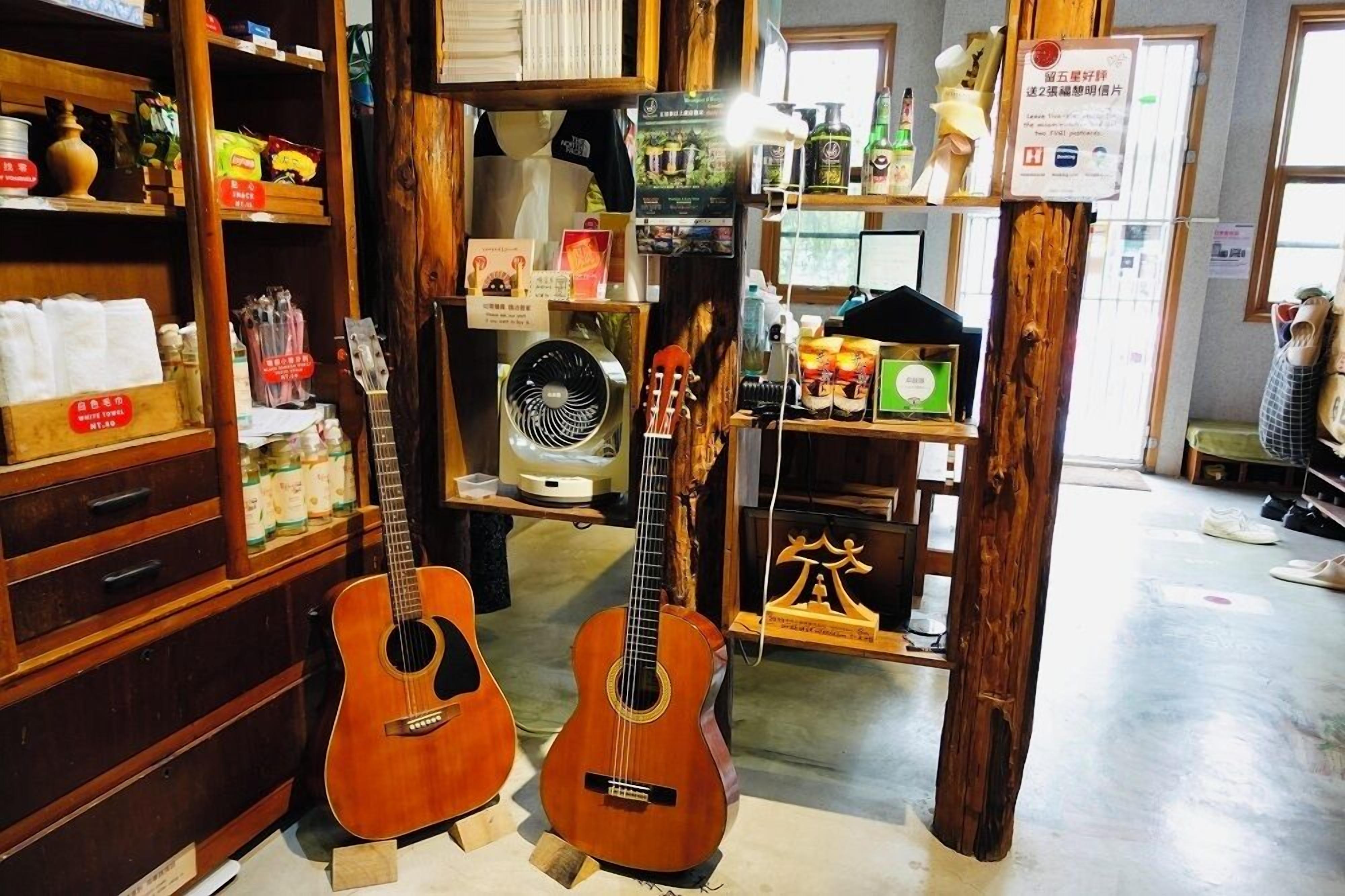 A room with wooden shelves displaying various items, two guitars, a fan, and a small shrine.