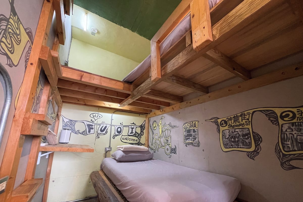 A compact room with a bunk bed, a small desk, and a wall with various drawings and text.