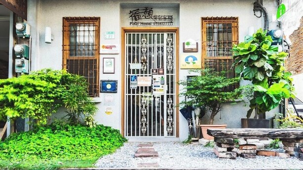 Un edificio tradicional japonés con entrada de madera, un portón metálico y un pequeño jardín con plantas y un sendero de piedras.