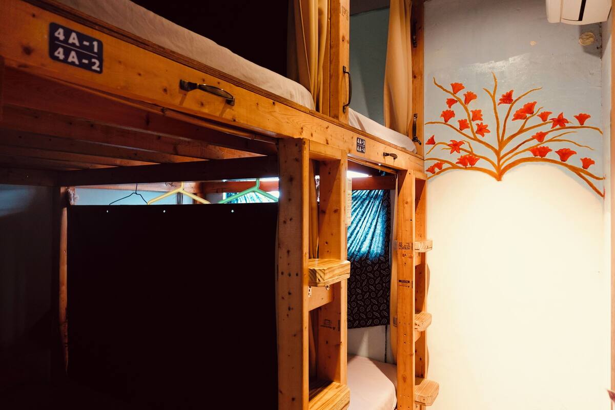 A wooden bunk bed with a mattress and a headboard, a small shelf, and a wall with a floral mural.