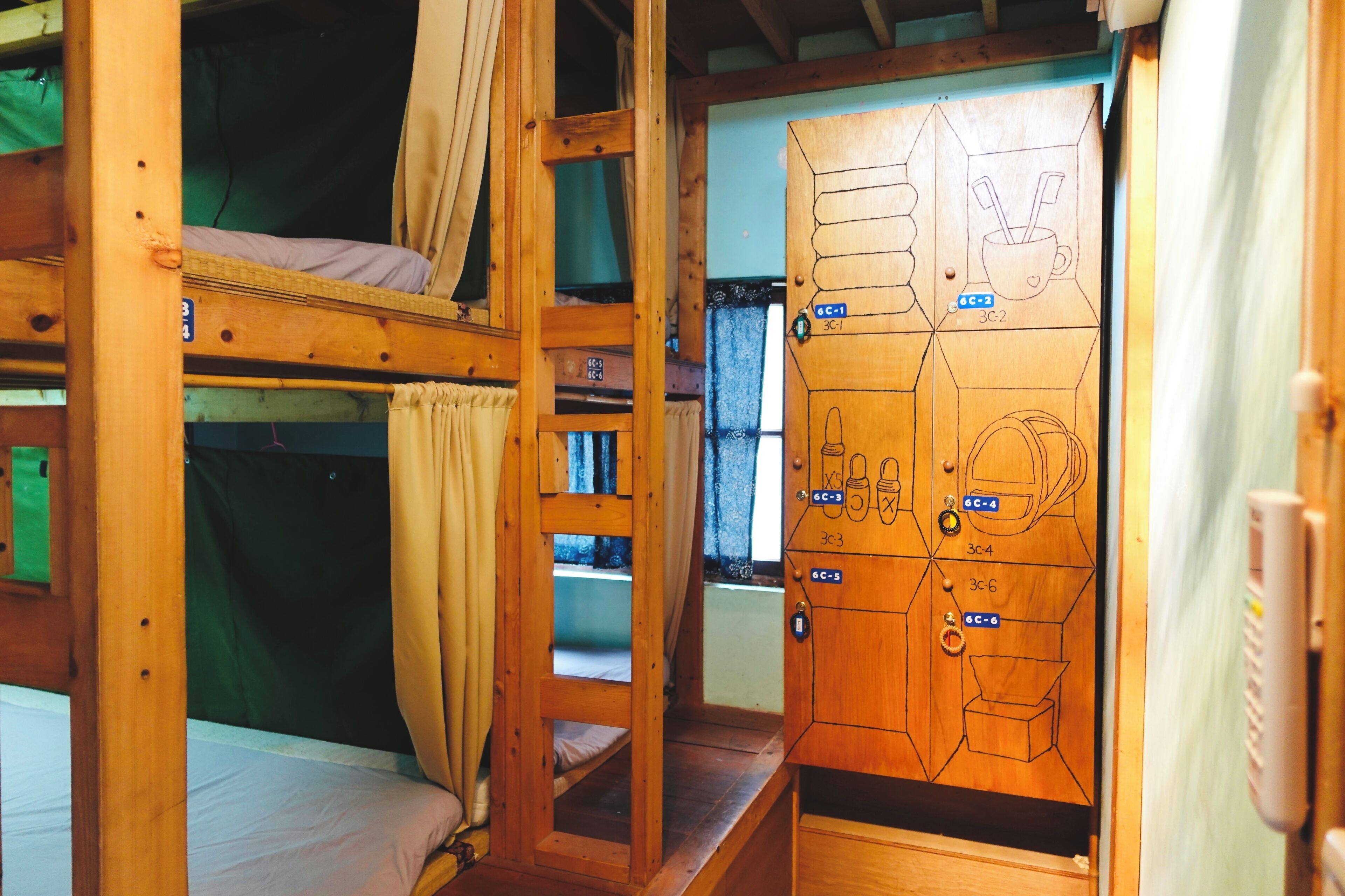 A wooden bunk bed room with a map on the door, a window with curtains, and a small table.