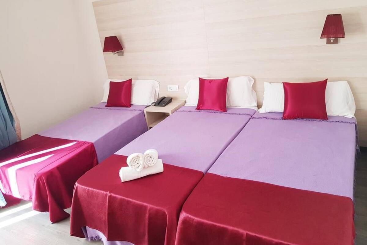 Een hotelkamer met twee bedden, elk met een rood en paars dekbed, en een tafeltje met handdoeken.