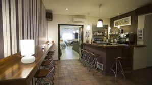 Zona de bar con una barra larga, taburetes e iluminación colgante.