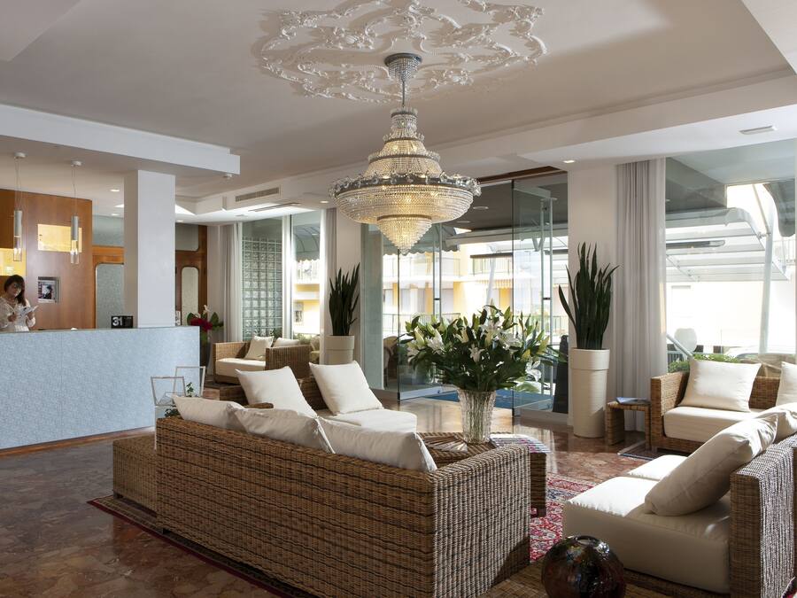 Un'ampia hall con reception, divani in vimini, un lampadario importante e vista esterna.