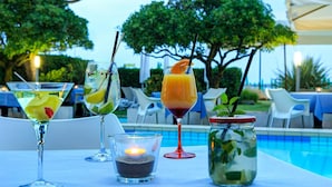 A table with three drinks, a candle, and a jar of mint leaves by a poolside. - Hotel Croce di Malta (Jesolo)