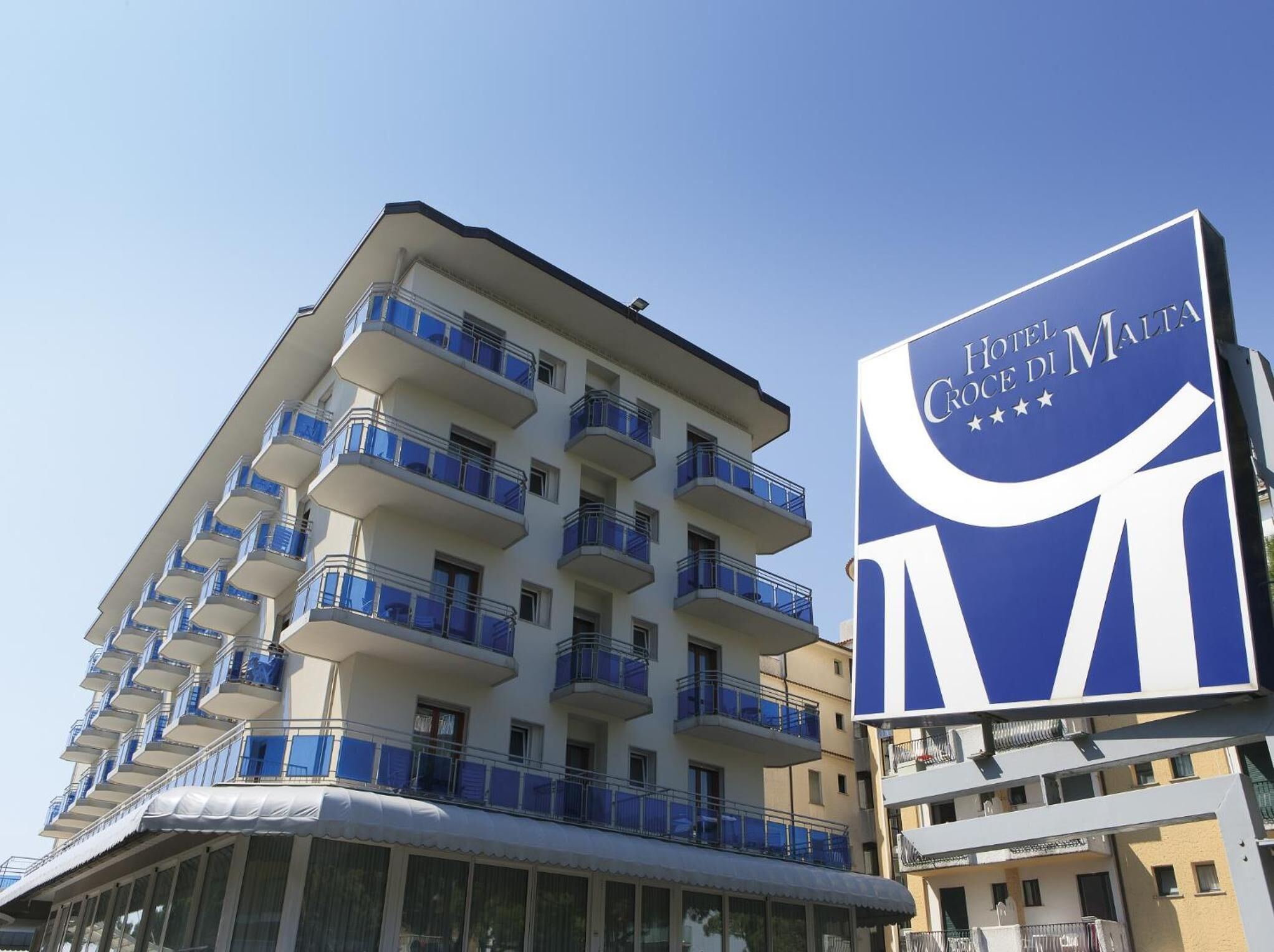 A hotel building with multiple balconies and a large sign for Hotel Croce di Malta.