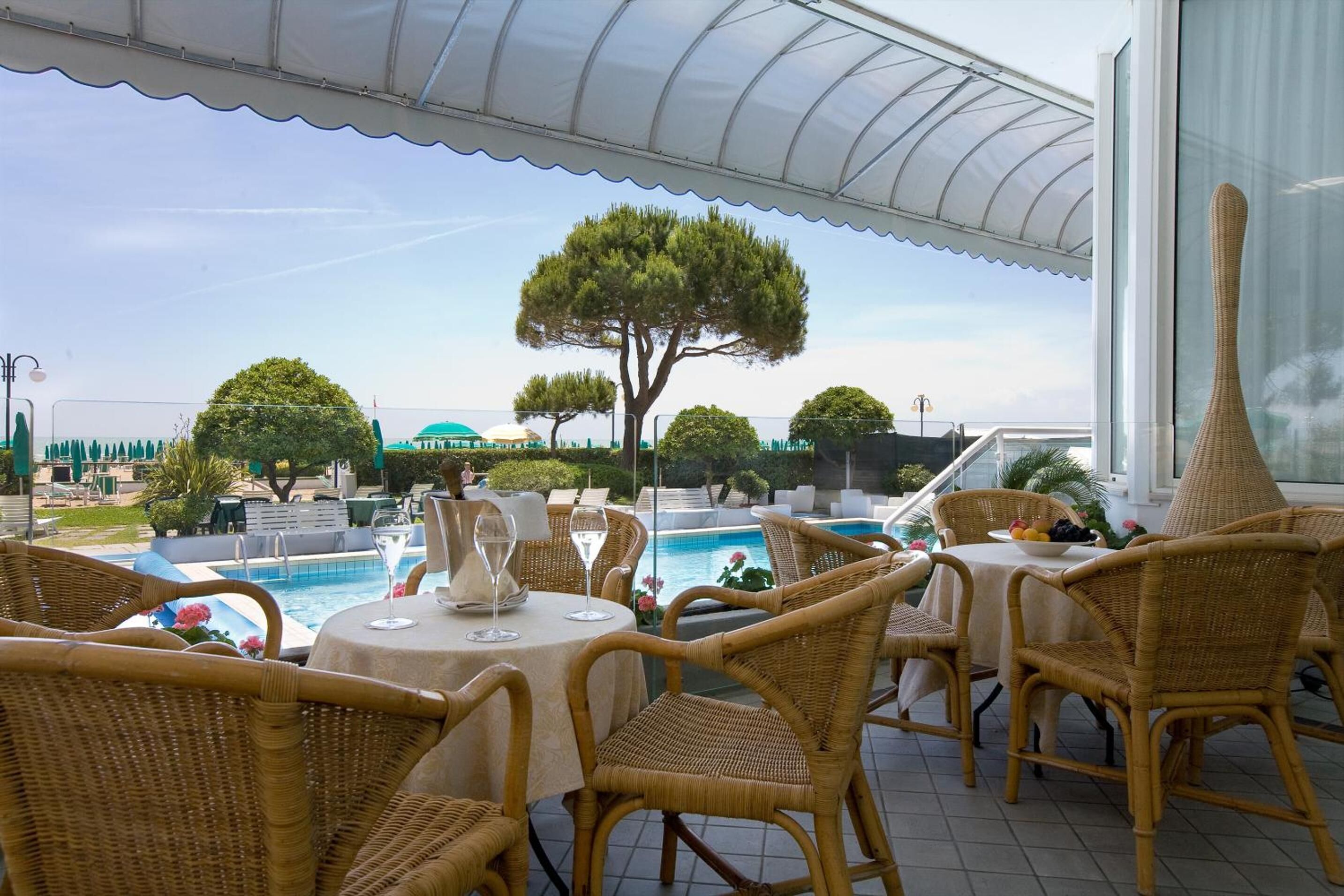 Un espace extérieur aménagé pour les repas, avec des chaises et des tables en osier, donnant sur une piscine et un jardin paysager.