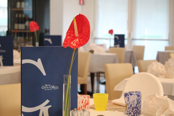Une chambre d’hôtel avec une enseigne bleue, un vase contenant une fleur rouge, une tasse jaune et une tasse à motifs bleus et blancs.