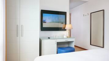Una camera d'albergo con un letto, una scrivania con una lampada, uno specchio grande e una TV che mostra una spiaggia.