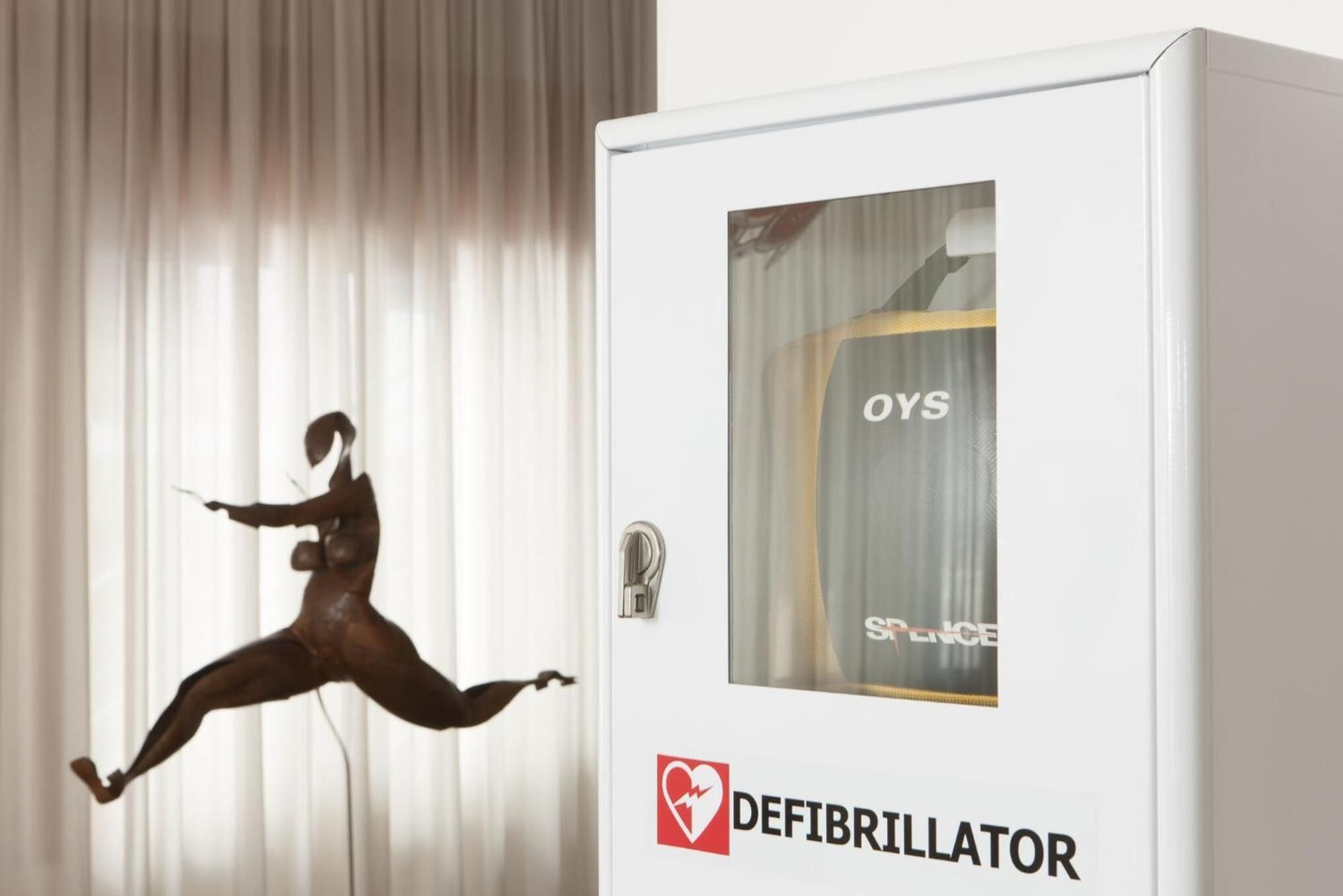 A defibrillator in a room with a curtain and a mannequin.