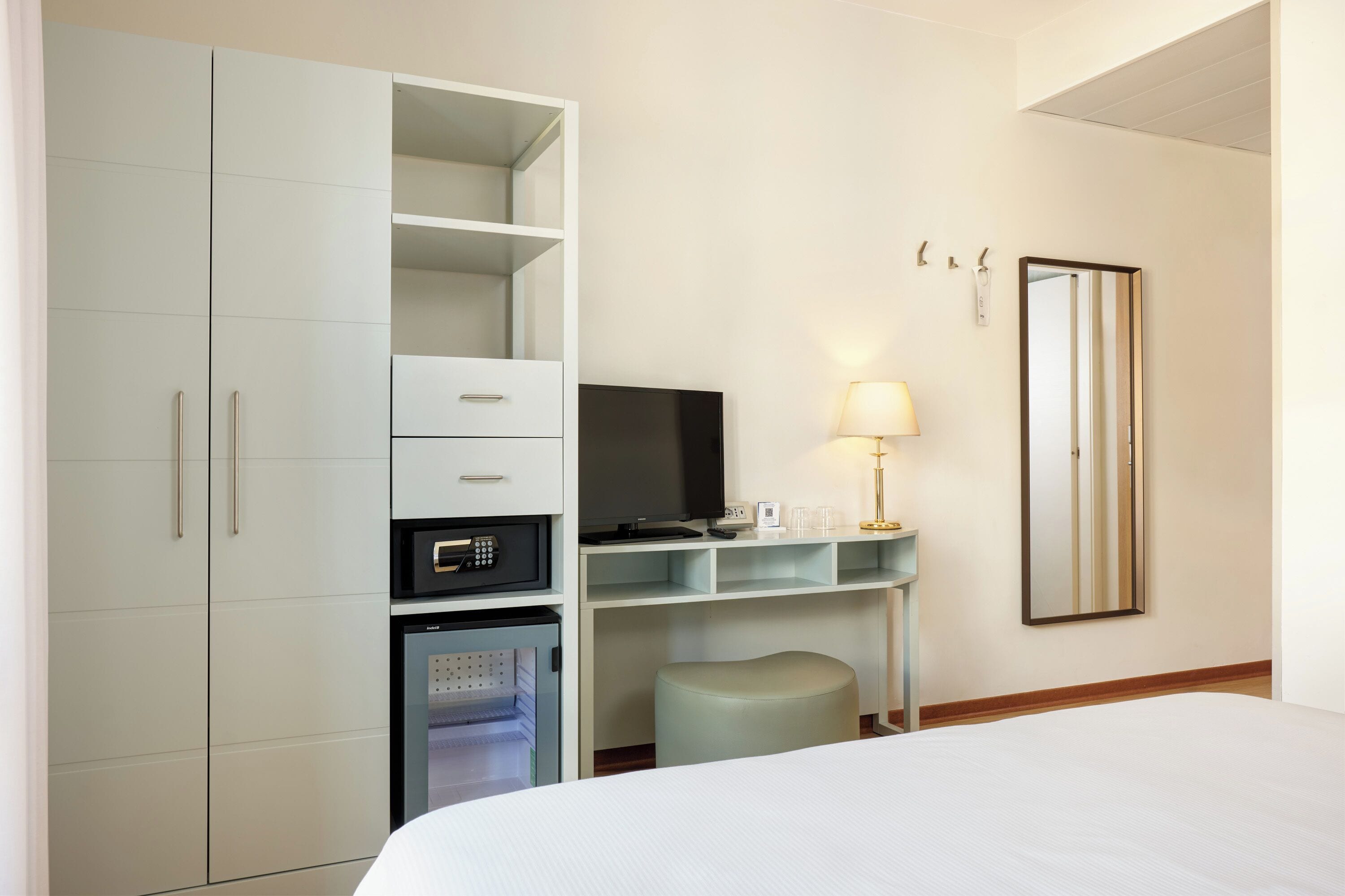 Una camera d'albergo con un letto, una televisione, un minibar, una scrivania con una lampada e un armadio.