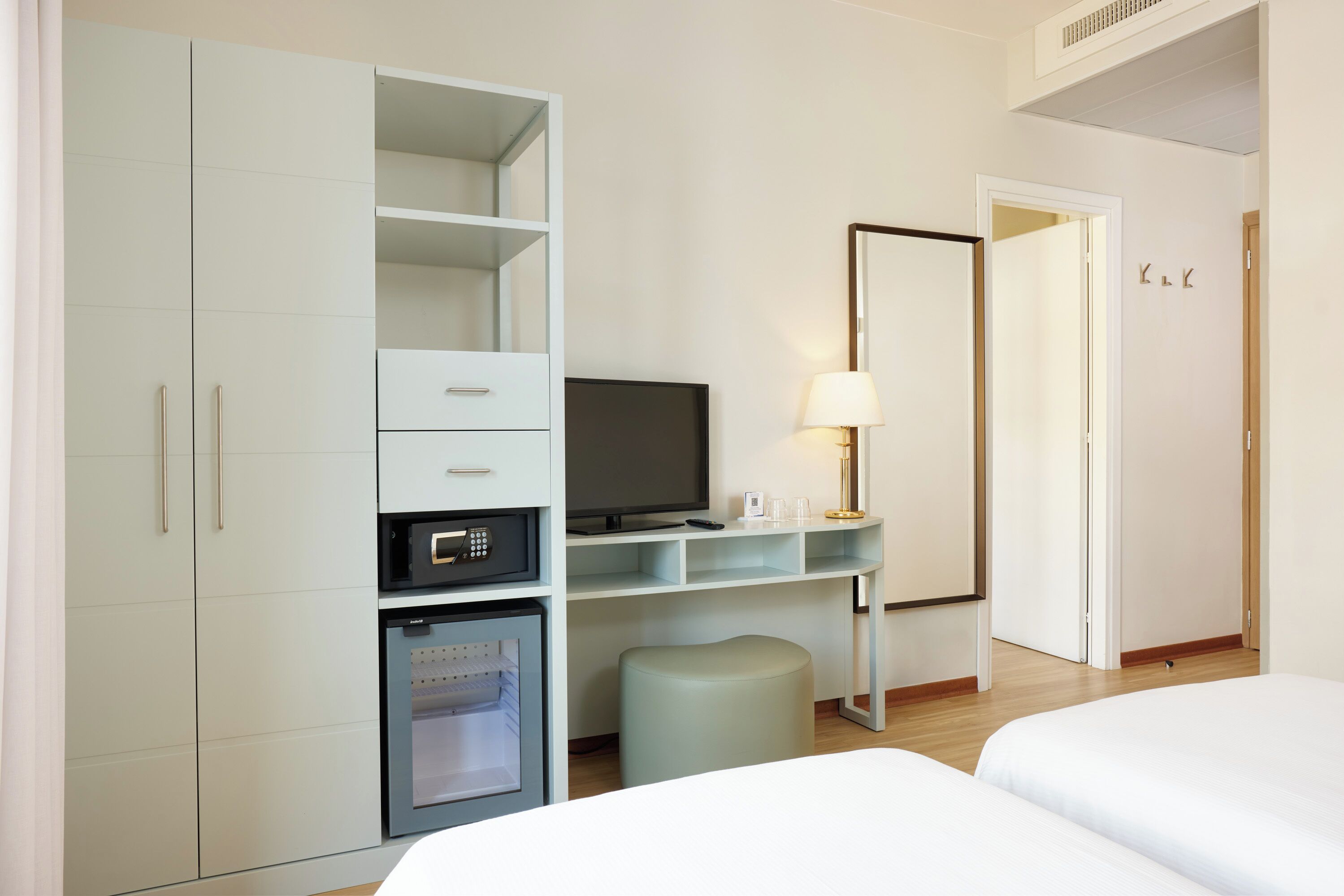 Habitación de hotel con cama, escritorio con televisor, un mini refrigerador y armario.