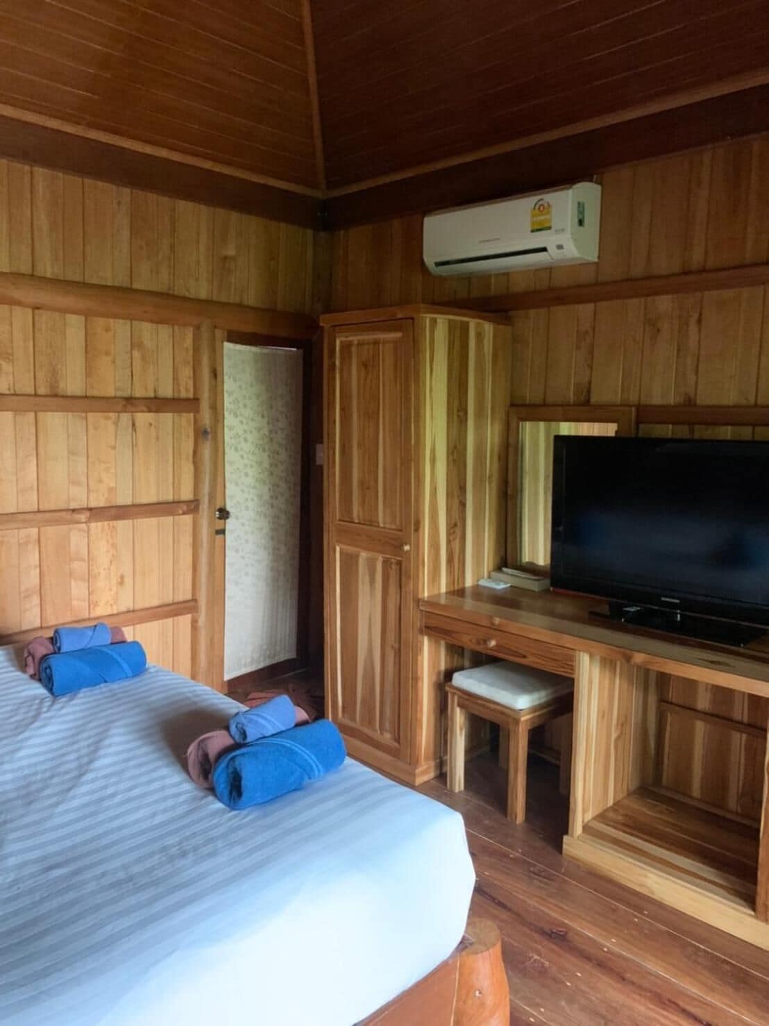 A wooden cabin room with a bed, a desk with a television, and an air conditioning unit.