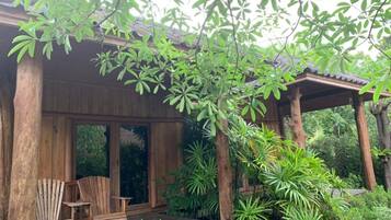 A wooden deck with two Adirondack chairs, surrounded by lush greenery and a wooden pergola.