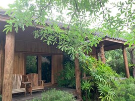 Una terraza de madera con dos sillas Adirondack, rodeada de abundante vegetación y un pérgola de madera.