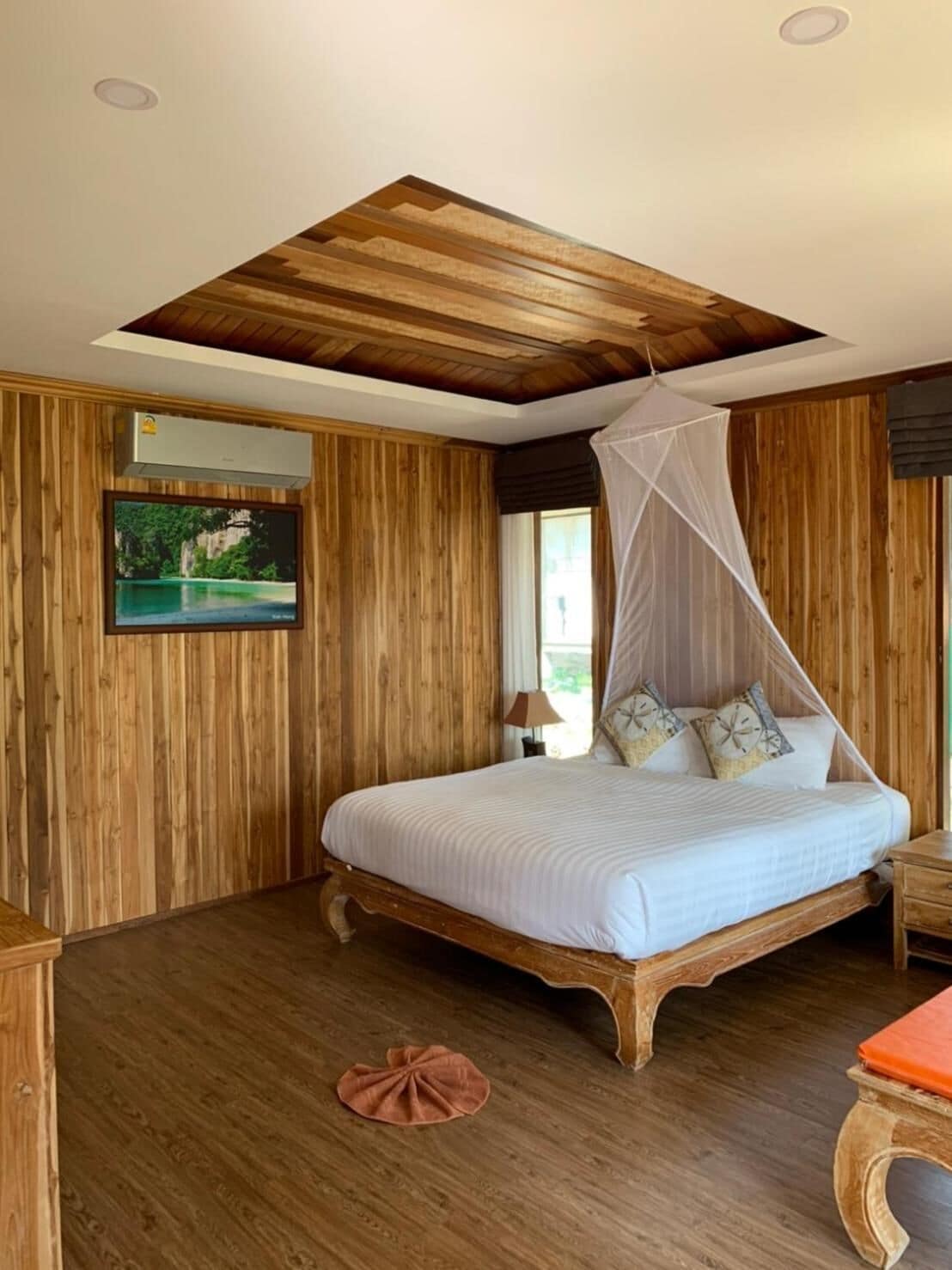 A wooden-paneled bedroom with a bed, a ceiling fan, and a mounted TV.