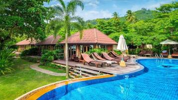 A pool area with lounge chairs and umbrellas, surrounded by lush greenery and a hilly landscape.