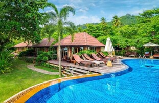 Zona de piscina con sillas de descanso y sombrillas, rodeada de exuberante vegetación y un paisaje montañoso.