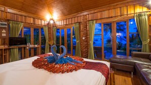 Una habitación con una cama grande, paredes de madera, televisión y vistas al exterior.