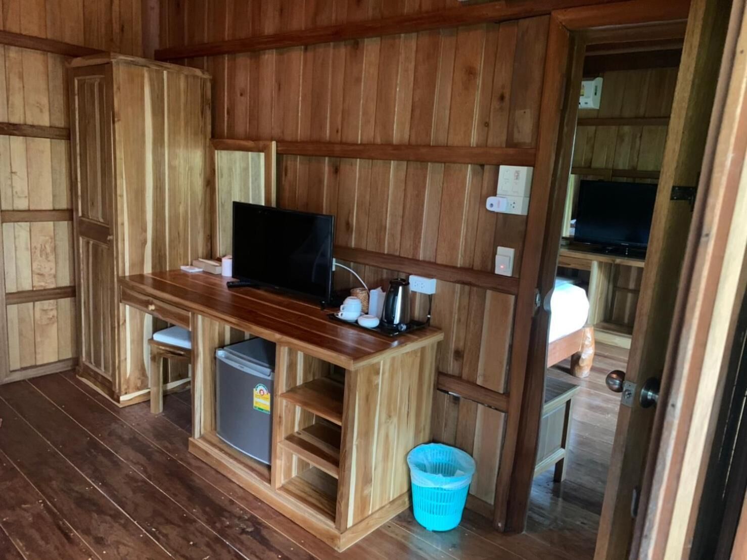 A wooden interior with a TV on a wooden table, a small fridge, and a trash bin.